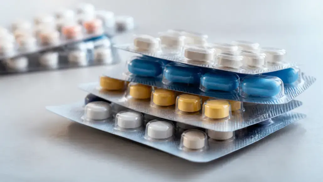 Stacked blister packs containing blue, yellow, and white pills on a reflective surface, ready for dispensing